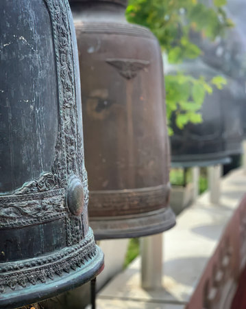 Metal bells hanging outdoors with blurred trees and buildings in background