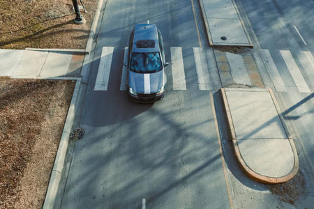 An aerial view of a silver car on a city street near a bus stop and sidewalk
