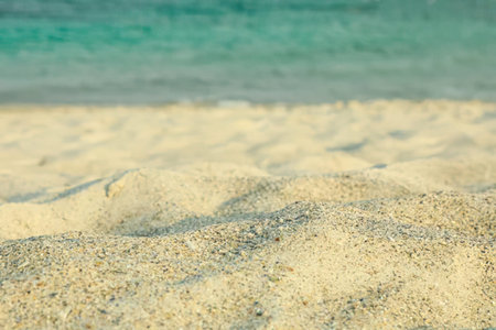 A natural scene showing textured sand and calm blue water in the background