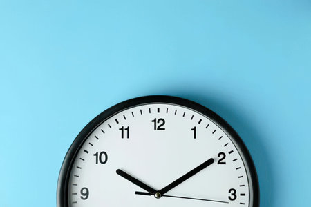 A simple round black clock on a blue wall showing time at 10:10