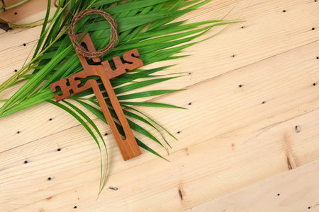 Simple image of a wooden cross with green leaves on a light wooden background.