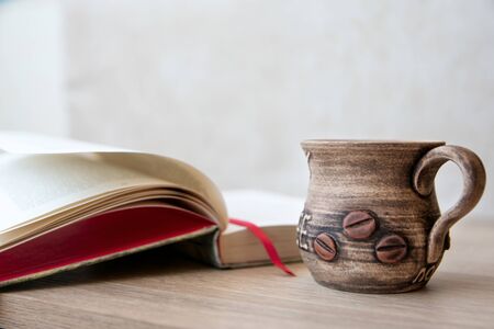 Cup of coffee with books on the table. Books in the house. Books and cup of coffee or tea on a wooden table. Cup of coffee with open book on the tableの写真素材