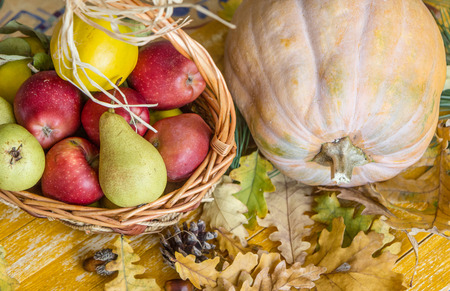 pumpkin and a basket of apples, quinces and pears on a wooden table with autumn leavesの写真素材