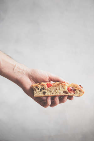 Hand holding a piece of focaccia. Italian focaccia with olives, tomato, carrot and thyme - homemade...