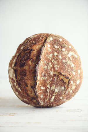 Baked bread of sourdough in hands. Artisan bread on light background. The bread of sourdough, homemade and natural creation. The sourdough has natural yeast, which makes the food healthier, as well asの写真素材