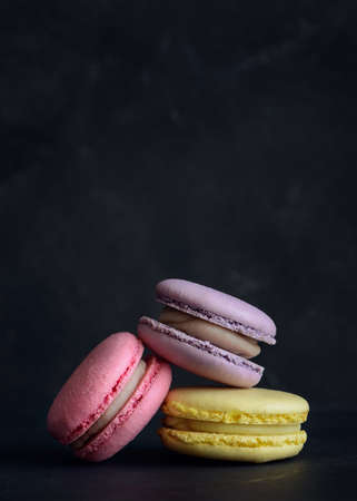 Stack of three macarons on dark background. Delicious pink, purple and yellow macaroons. Vertical photos. Copyspace.の写真素材