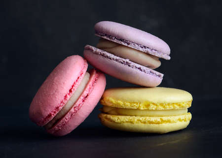Stack of three macarons on dark background. Delicious pink, purple and yellow macaroons. Horizontal photos. Macaron close-up.の写真素材