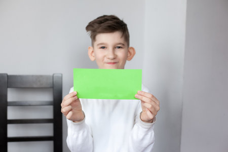 Funny boy holding sheet of green paper for your text. smiling child showing empty green card for simple textの写真素材