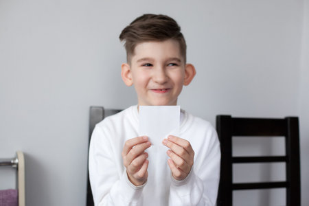 Funny boy holding sheet of white paper for your text. Blurred smiling child showing empty white card for simple textの写真素材