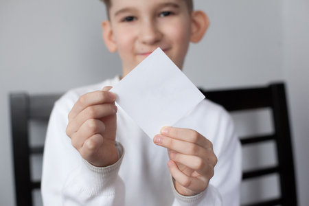 Cropped photo of blurred funny boy holding sheet of white paper for your text. Smiling child showing empty white card for simple textの写真素材