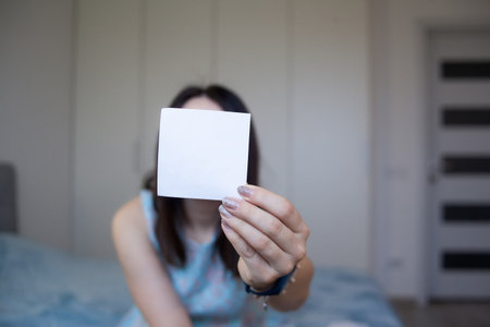 Woman holding sheet of white paper for your text. Blured girl showing empty white card for simple textの写真素材