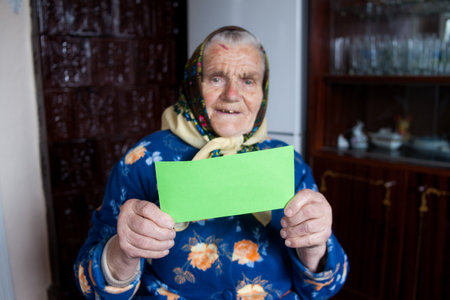 Old woman holding sheet of green paper for your text. Blurred elderly woman showing empty green card for simple textの写真素材
