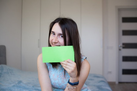 Smiling girl holding sheet of green paper for your text. Happy woman showing empty white card for simple textの写真素材
