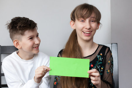 Girl and boy holding sheet of green paper for your text. smiling sister and brother showing empty green card for simple textの写真素材