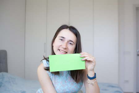 Woman holding sheet of green paper for your text. Smiling girl showing empty green card for simple textの写真素材