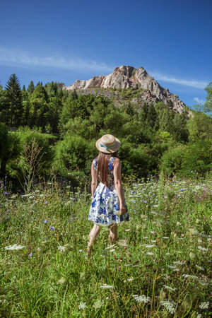 Stylish girl in straw hat traveling on sunny mountains. Young beautiful woman with beautiful hair exploring mountains and walking in light. Travel and wanderlust. Amazing momentの写真素材