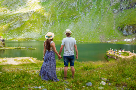 A beautiful young couple holding hands each other on the shores of Lake Balea against the background of the high Romanian mountains. exciting holidays in mountains in Transylvania, Romaniaの写真素材