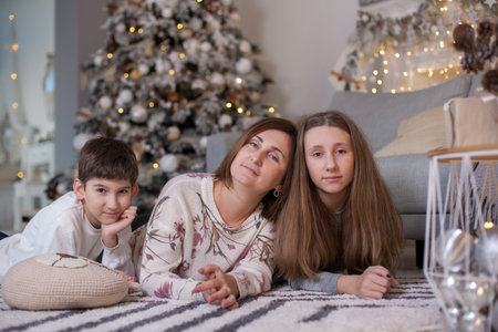 happy family lying on floor near sofa and christmas tree with presents and looking at camera. Mother, daughter and son at Christmas time. Merry Christmas and Happy New Yearの写真素材