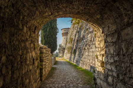 Brescia, Italy - December, 2015: Big tower in the Medieval castle of the city Brescia on a sunny clear day against a bright blue sky. Part of Brescia castle. view from the arch. Castello di Bresciaのeditorial素材