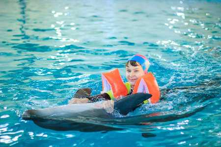 Dolphin therapy. Happy little girl swimming with dolphins in Dolphinarium. Swimming, bathing and communication with dolphins. Treatment of children by means of dolphins. Concept People and dolphins.の写真素材
