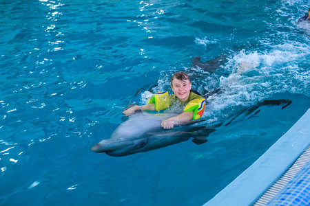 Treatment of children by means of dolphins. Dolphin therapy. Happy little girl swimming with dolphins in Dolphinarium. Swimming, bathing and communication with dolphins. Concept People and dolphins.の写真素材