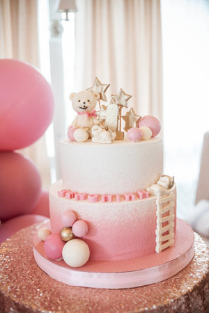 Two-tier white pink cake with number one, little bear, white and pink balls and golden stars on a table with a sparkle tablecloth. Concept of a birthday cake for a girl on her first birthday.の写真素材