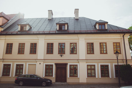 Przemysl, Poland - October, 2016: Beige house with brown windows, old wooden door, grey roof with small windows, street lantern, green bush and black car in front of it. View of building in Przemysl.のeditorial素材