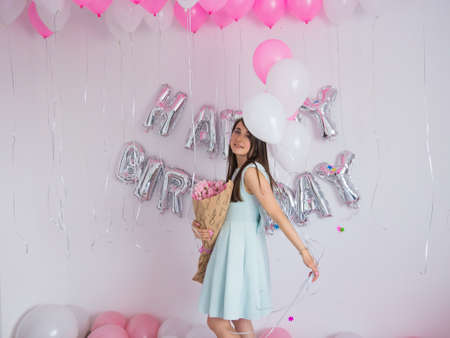 Brunette woman in mint dress holding bouquet of tulips. Birthday decorations with white and pink...