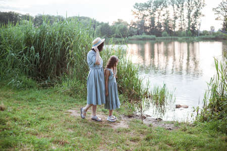 A woman and a girl stands on the shore of the lake and looks at nutria in the water. Family watching with interest on coypu swimming. Mom and daughter contemplating Myocastor coypus in public park.の写真素材