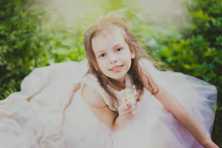 A girl in white dress sniffs a bouquet of daisies in spring cherry garden. Portrait of child among...
