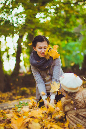 Beautiful young mother and her happy daughter are having fun in the forest at autumn. Walks in an...
