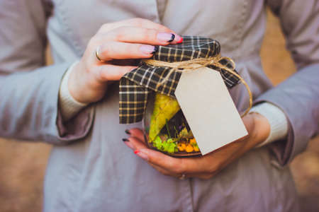 Cropped photo of woman holds glass jar filled with yellow and green leaves, berries and seeds with...