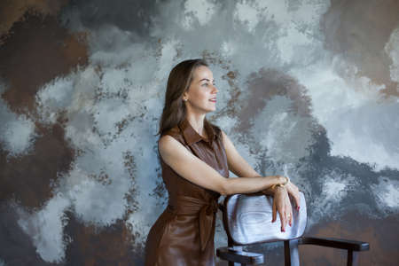 Portrait of a beautiful young business woman with brown hair in a brown dress. Side view of happy...