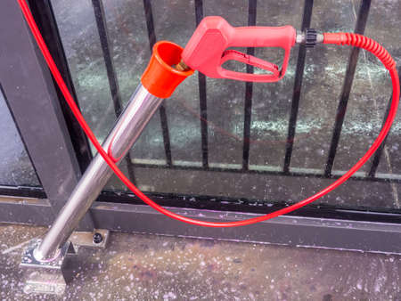 Red handle of car wash high pressure water gun with long nozzle inserted into metal cylinder. The...