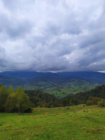 Carpathian landscape with cloudy sky. A green meadow in mountains near old forest. Lifestyle in the Carpathian village. Ecology protection concept. Explore the beauty of the world.の写真素材