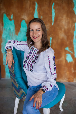 Beautiful sensual girl with brown hair in blue jeans and white blouse sits on blue chair with...