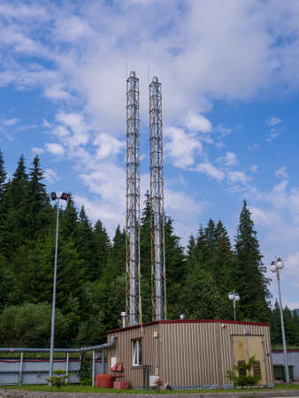 Modern small boiler house with two big pipes against the blue sky and green forest in sunny summer...