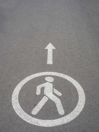 Circular white traffic sign. Asphalt road for pedastrians marked with special sign. White Pedestrian Symbol Painted over gray Asphalt with Arrow. Permission to move people. Signs drawn on the pavementの写真素材