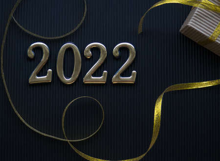 2022 on the black background. 2022 gold figures lie next to a small gift in a craft brown wrapper...