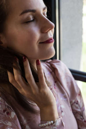 Beautiful young woman in pink dress resting on the windowsill. Portrait of happy smiling girl sits on the stained glass window at industrial loft wooden brick style interior. Leisure concept.の写真素材