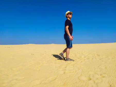 Young woman in white blouse and brown shorts going in desert under blue sky. Girl walking in the sand dunes in the Ukrainian desert, Oleshky Sands nature park, Oleshkivski pisky, Kherson oblastの写真素材