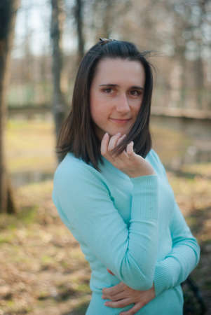 Portrait of a darkhead girl outside in early spring. A beautiful black hair young woman in mint color clothes outdoor on the blurred park background. Happy smiling girl touching her face.の写真素材