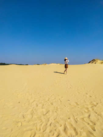 Young woman in white blouse and brown shorts going in desert under blue sky. Girl walking in the...