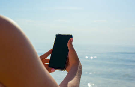 Close up photo of girls hands holding phone against the sea background. Woman taking picture of...
