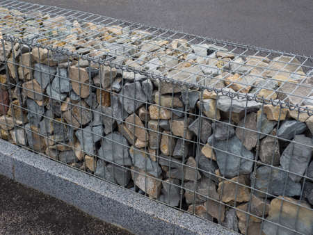 Decorative fence of bulk stone in the grid. Textured background of a stone wall with iron netting. Stone wall in wire frame. Gabion filled with limestoneの写真素材
