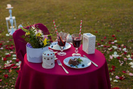 Romantic table for two outdoors with a red tablecloth and covers on chairs, with desserts, mulled...