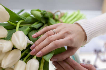 Girl trying on a ring in a jewelry store with white tulips bouquet background. Jewelry and shopping concept. Young woman is choosing ring in the shopping mall. Concept of consumerism, sale, rich life.の写真素材