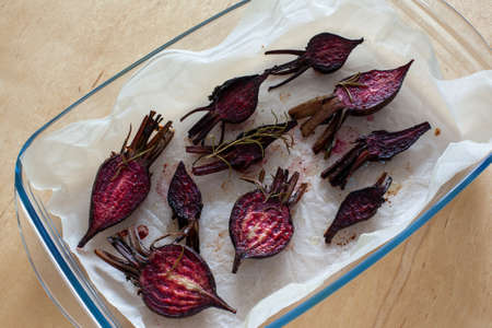 Glazed and roasted young beets on a piece of baking paper, baked baby beets on the wooden background. Roasted young half beets with greens and sea salt in baking tray.の写真素材