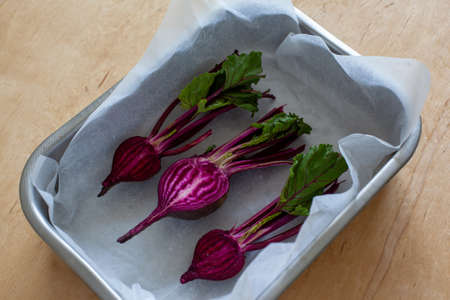 Red beets prepared for baking, baby beets on the wooden background. Young half of beet in baking...