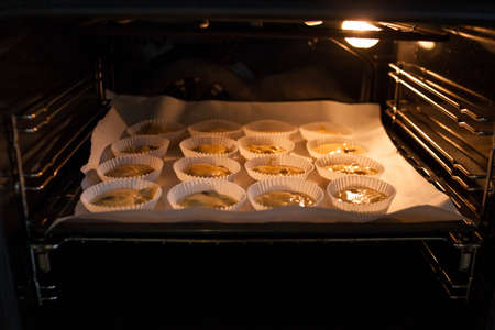 Paper cases filled with muffin dough baking in oven. Making of muffins with raisins. Homemade baking. Step for making muffins, pie, biscuit. Baking process step by step.の写真素材